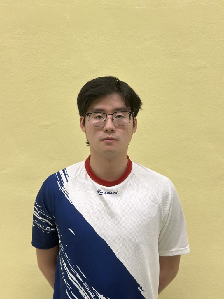 Sportler mit schwarzem Haar und Brille (Chenyang Jiang) steht vor grauer Wand und trägt weißes Trikot mit blauem diagonalem Muster und rotem Kragen